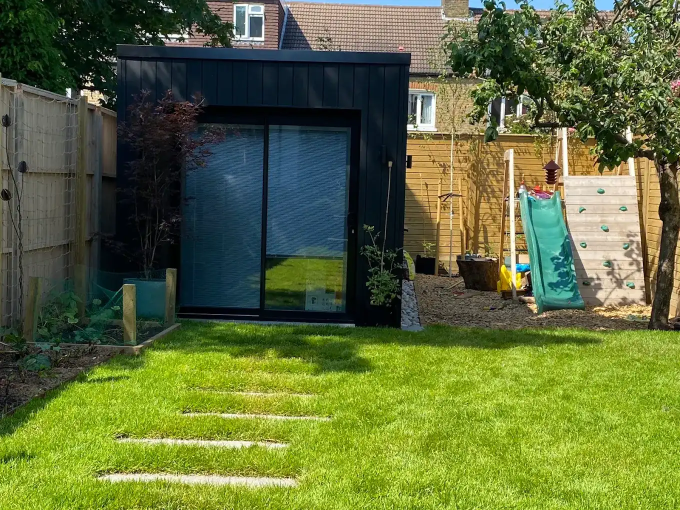 A black-clad garden studio in Brixton with a north-facing rooflight, used as a creative workspace.