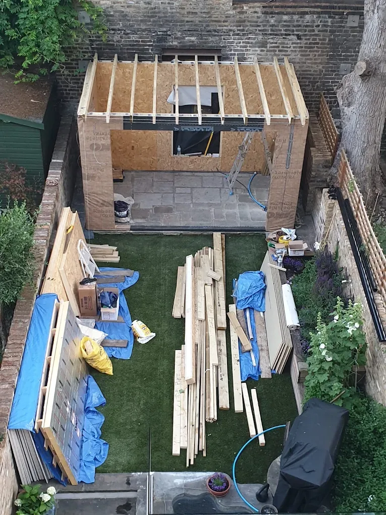 A garden office frame under construction in a walled London garden.