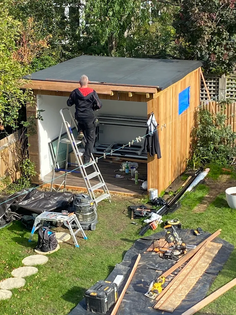 Jakub on site, finishing the roofline of a cedar-clad garden office.