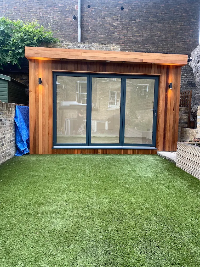 A cedar garden office with bi-fold doors at the end of a walled London garden.